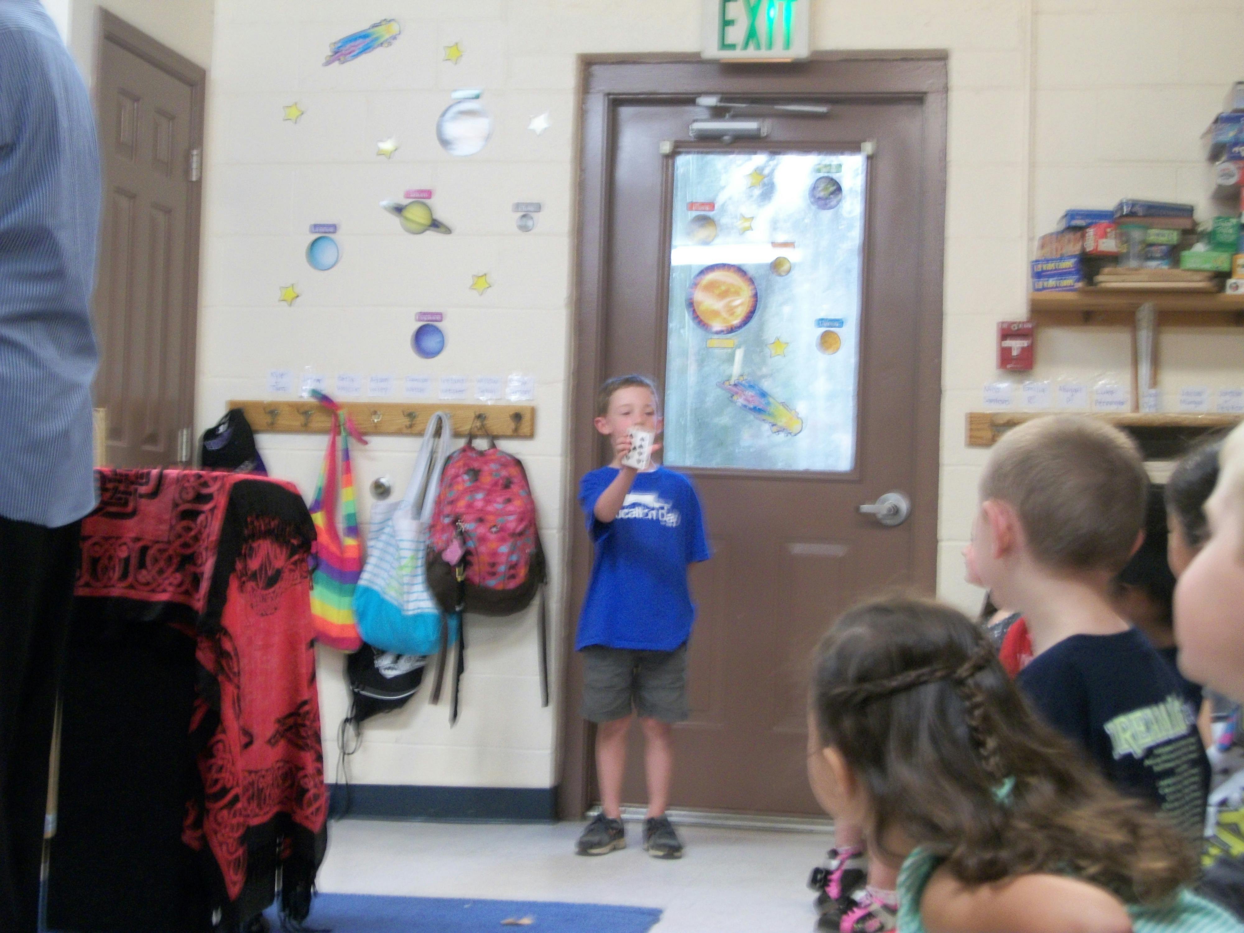 Child in blue shirt holding a cup, facing other children