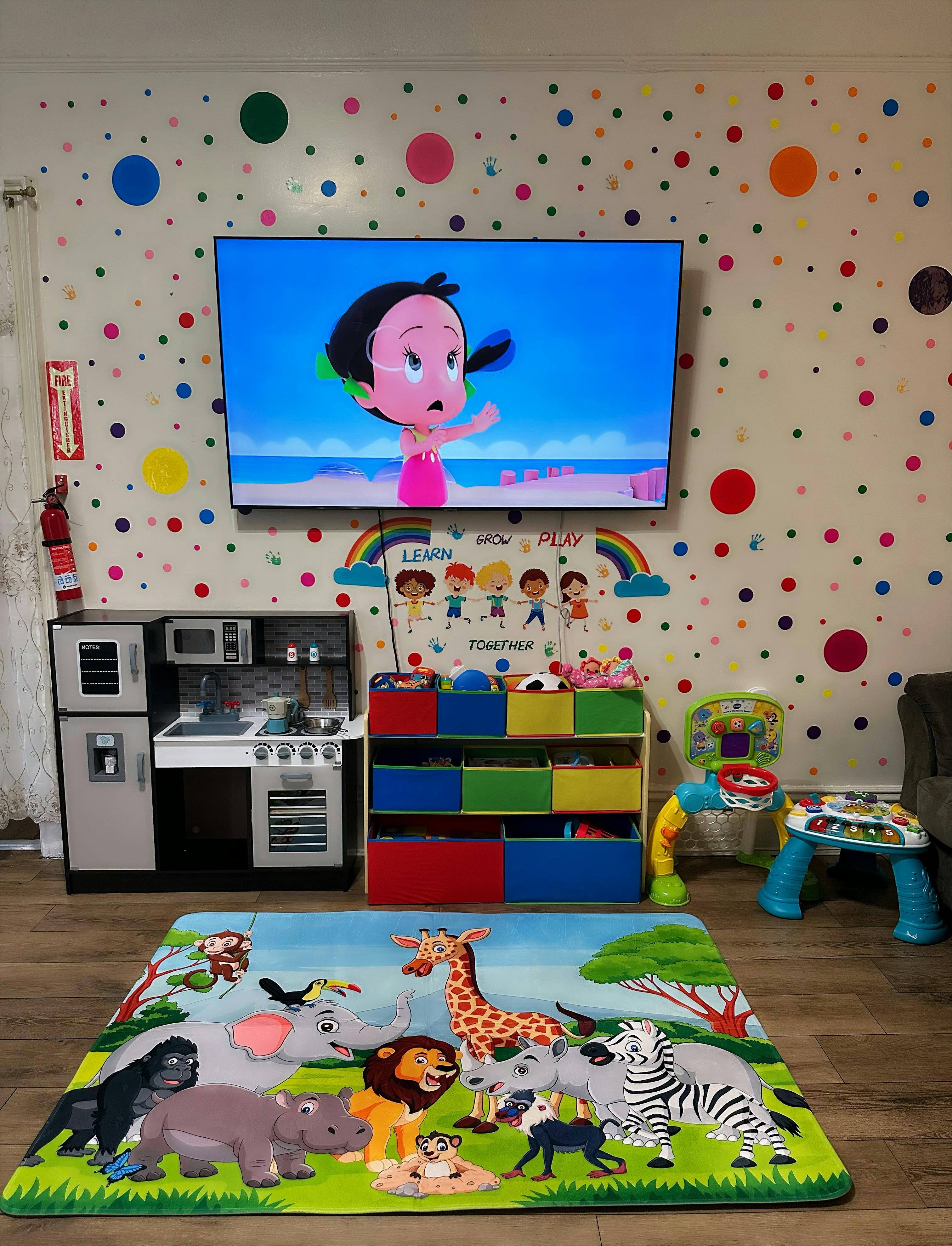 Playroom with a TV showing a cartoon, toy kitchen, and animal-themed rug