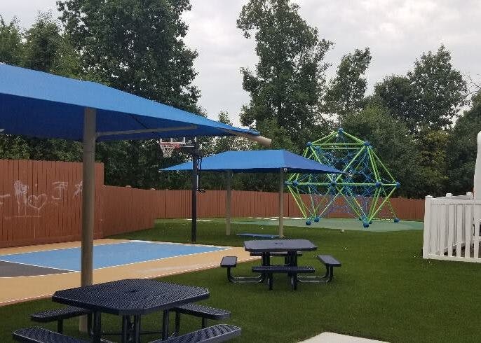 Outdoor playground with blue umbrellas, picnic tables, and climbing dome