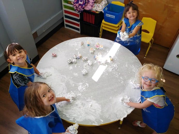 Four children playing with white material on a round table