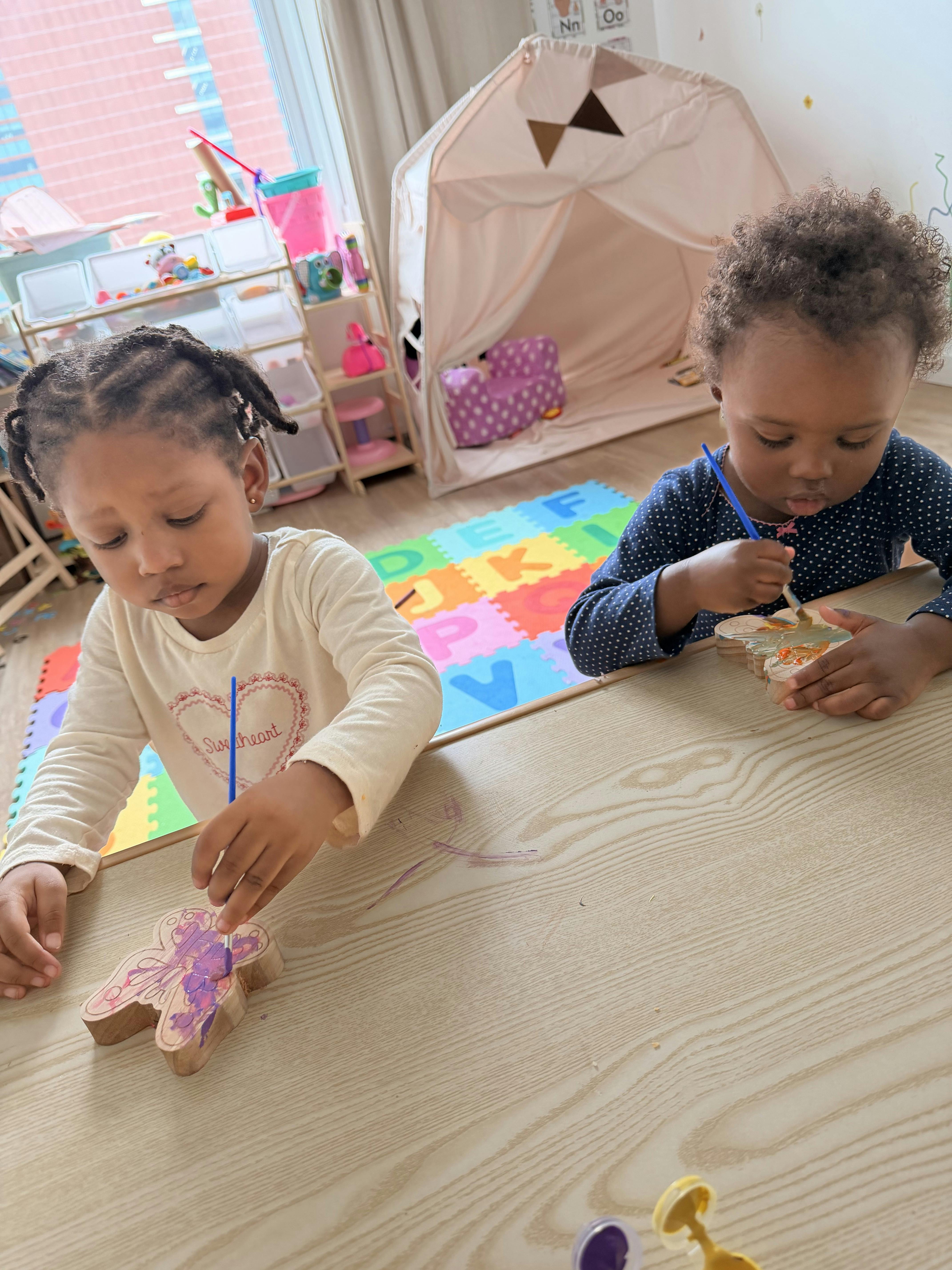 Two children painting wooden butterfly cutouts at a table