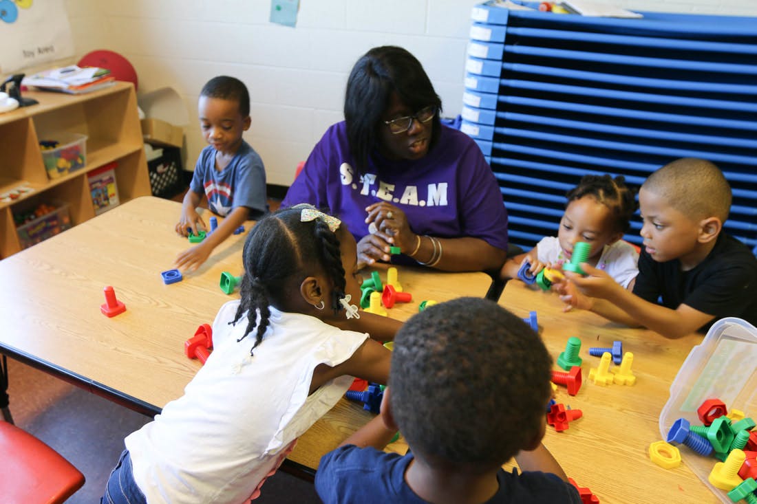 Adult and multiple children playing with colorful building blocks at a table
