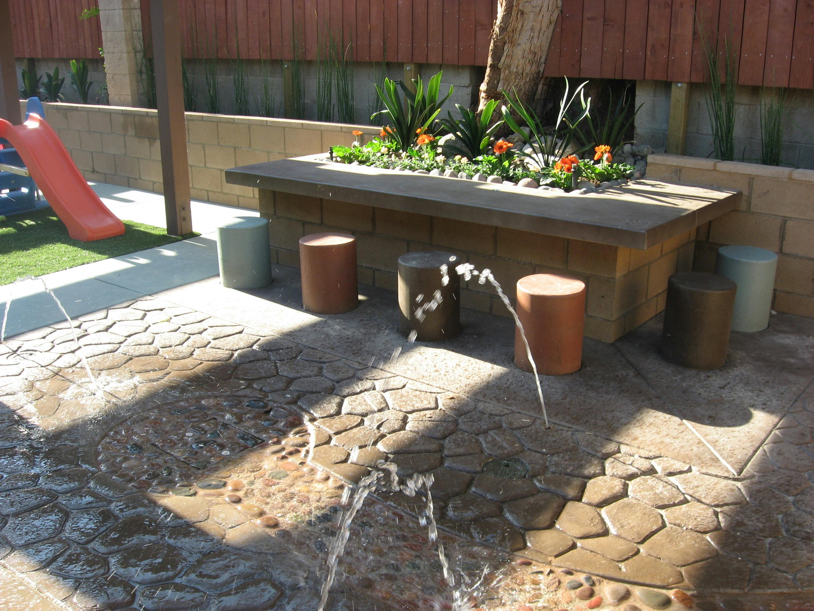 Water jets splashing on a patio with a bench and small stools