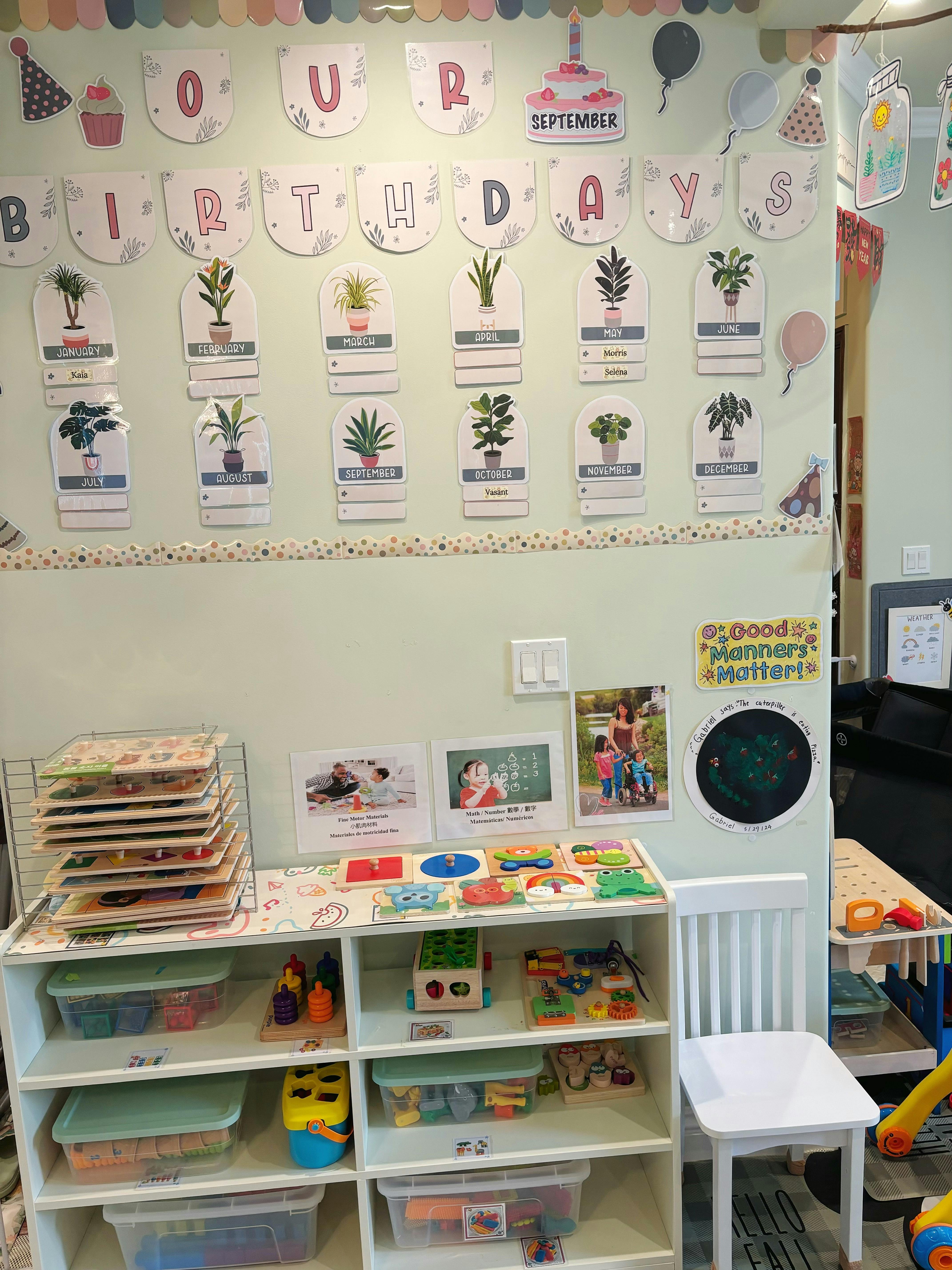 Classroom wall with birthday banner, plant cards, and shelves with puzzles and toys