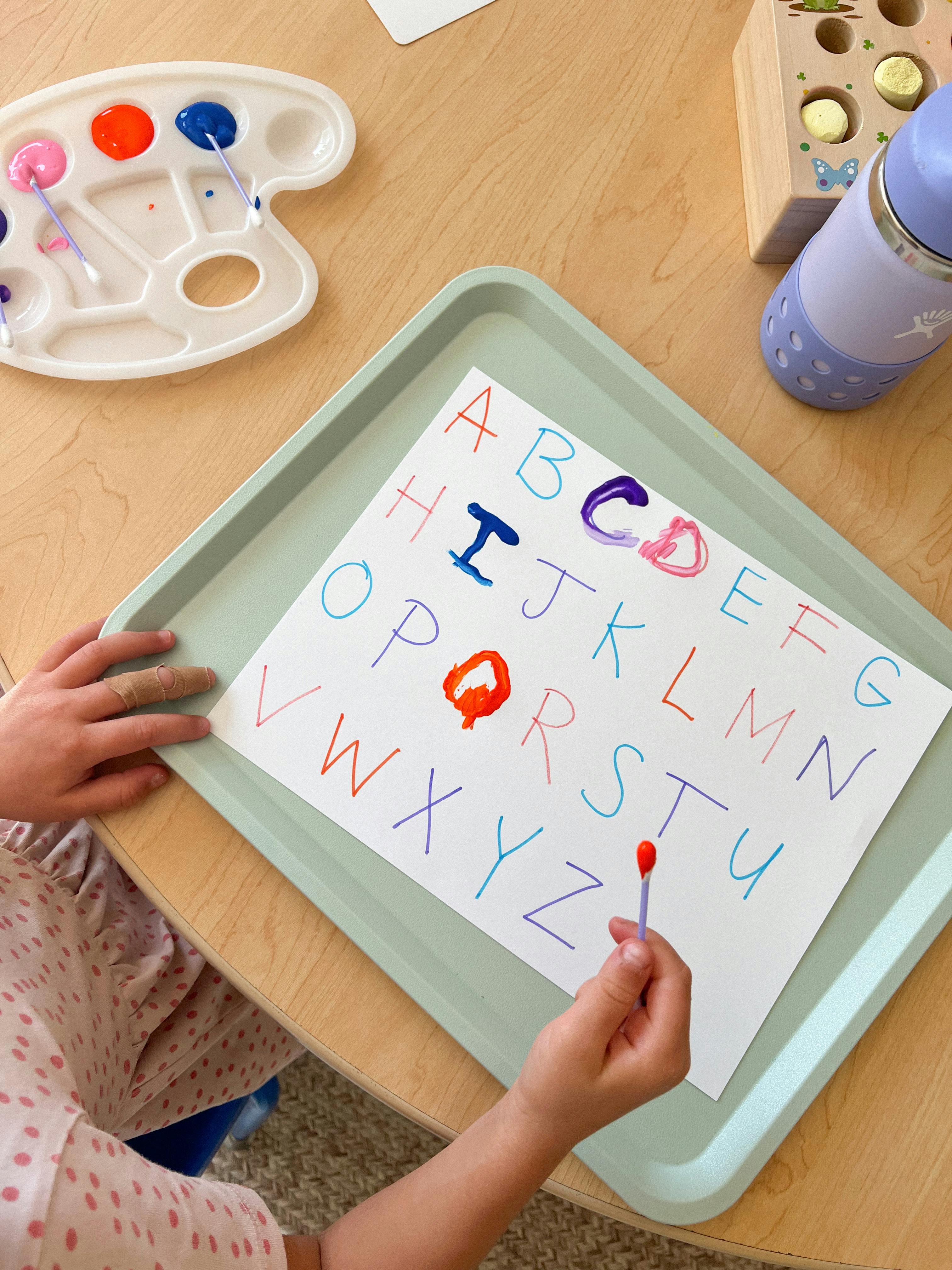 Child painting letters on a paper with a cotton swab