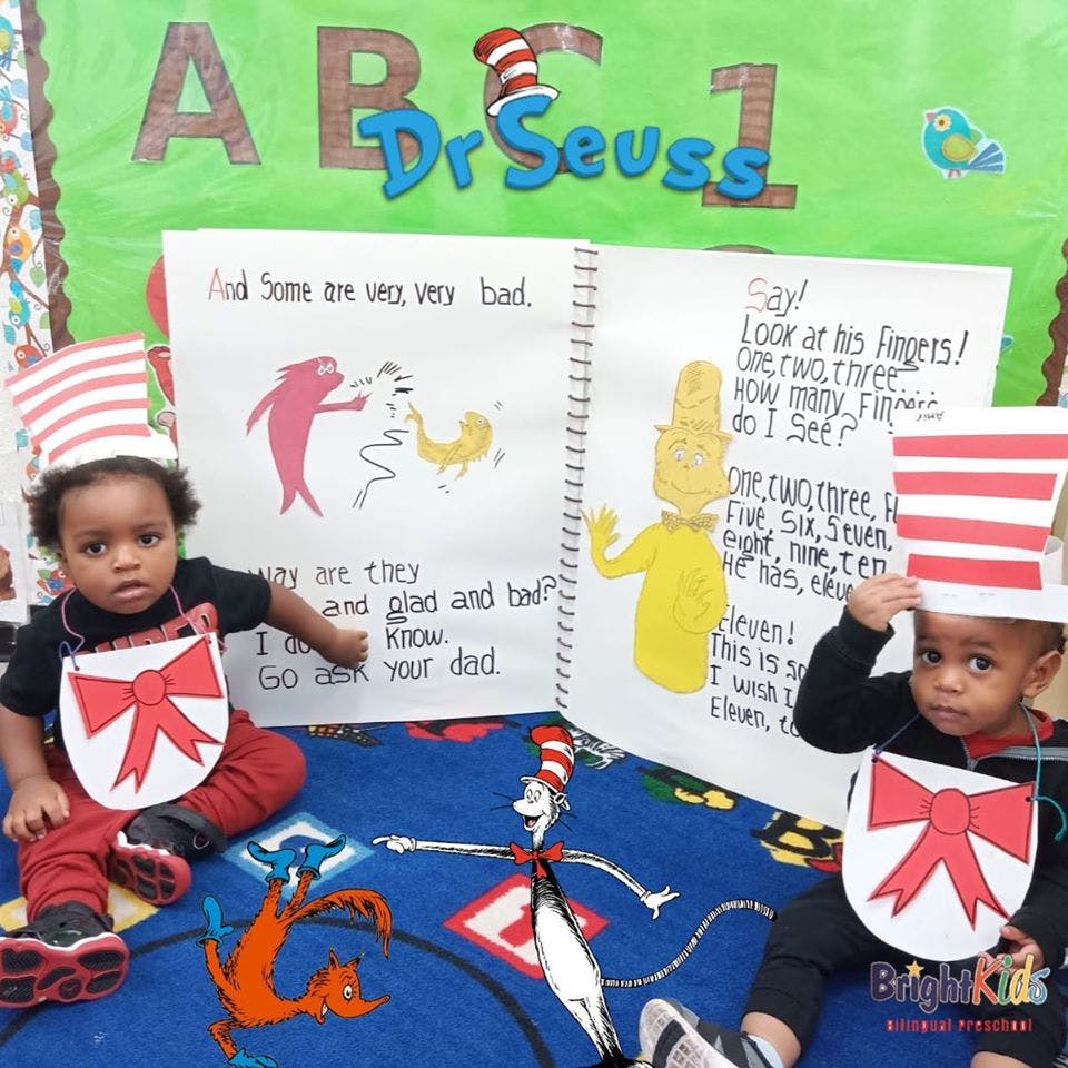 Two children wearing Dr. Seuss hats and bibs sitting on a Dr. Seuss rug