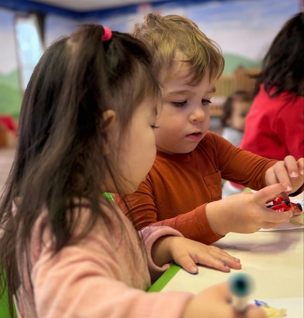 Two children playing with a small toy car at a table