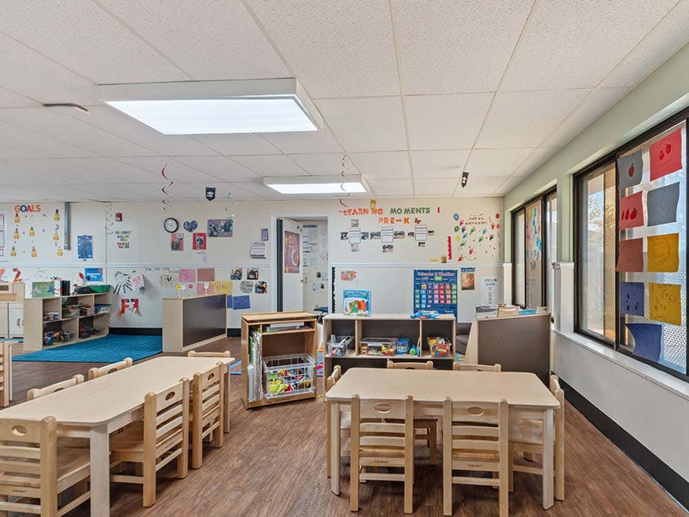 Empty classroom with small tables and chairs, and colorful artwork on walls
