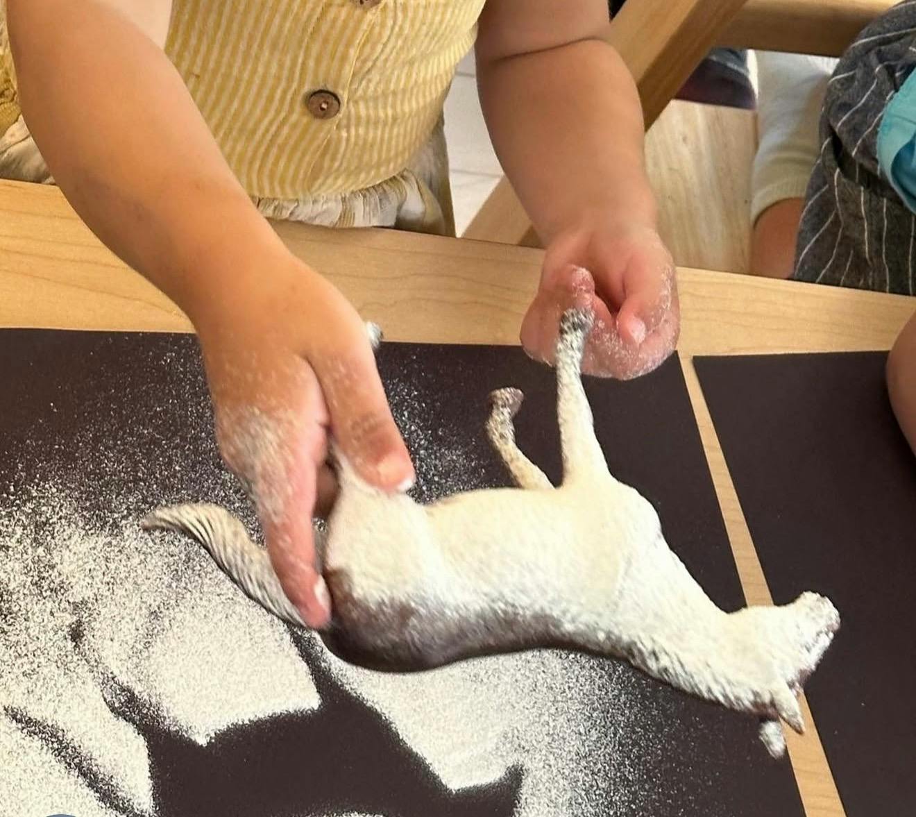 Child playing with a toy horse in white powder on a dark surface