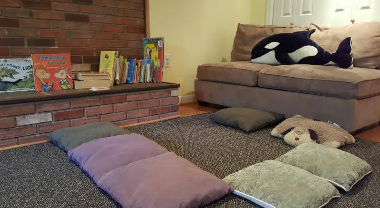 Floor cushions and pillows on a rug in a room with a couch and books