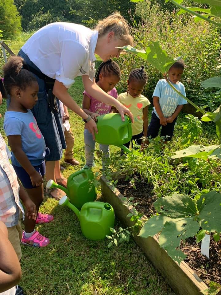 Adult and children watering plants in a garden bed with green watering cans