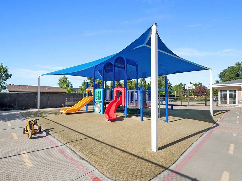 A colorful playground with slides and climbing structures under a large blue shade
