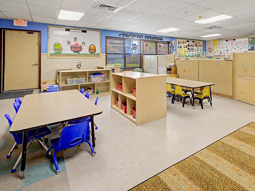 Empty preschool classroom with small tables and chairs