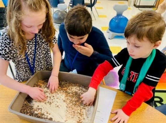 Three children playing with sand and seeds in a tray