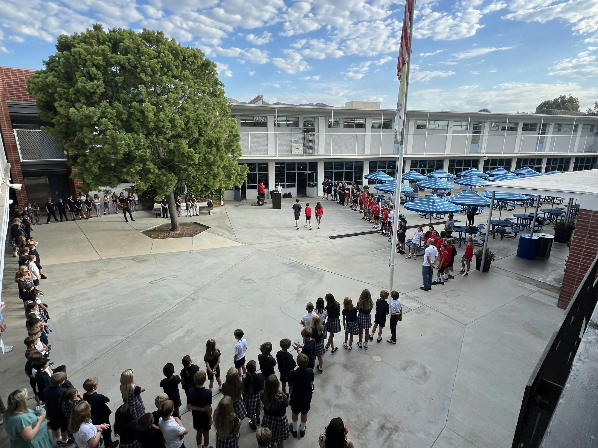 Students gathered in a courtyard with a flagpole and building in the background