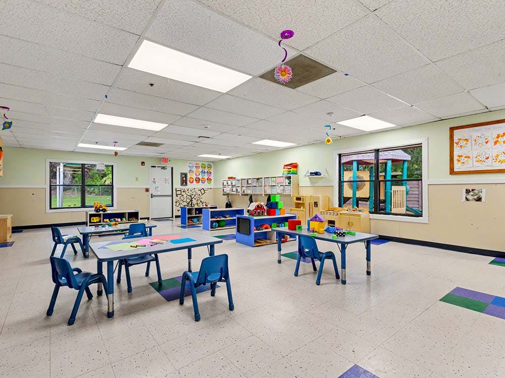 Classroom with child-sized tables and chairs, shelves with toys