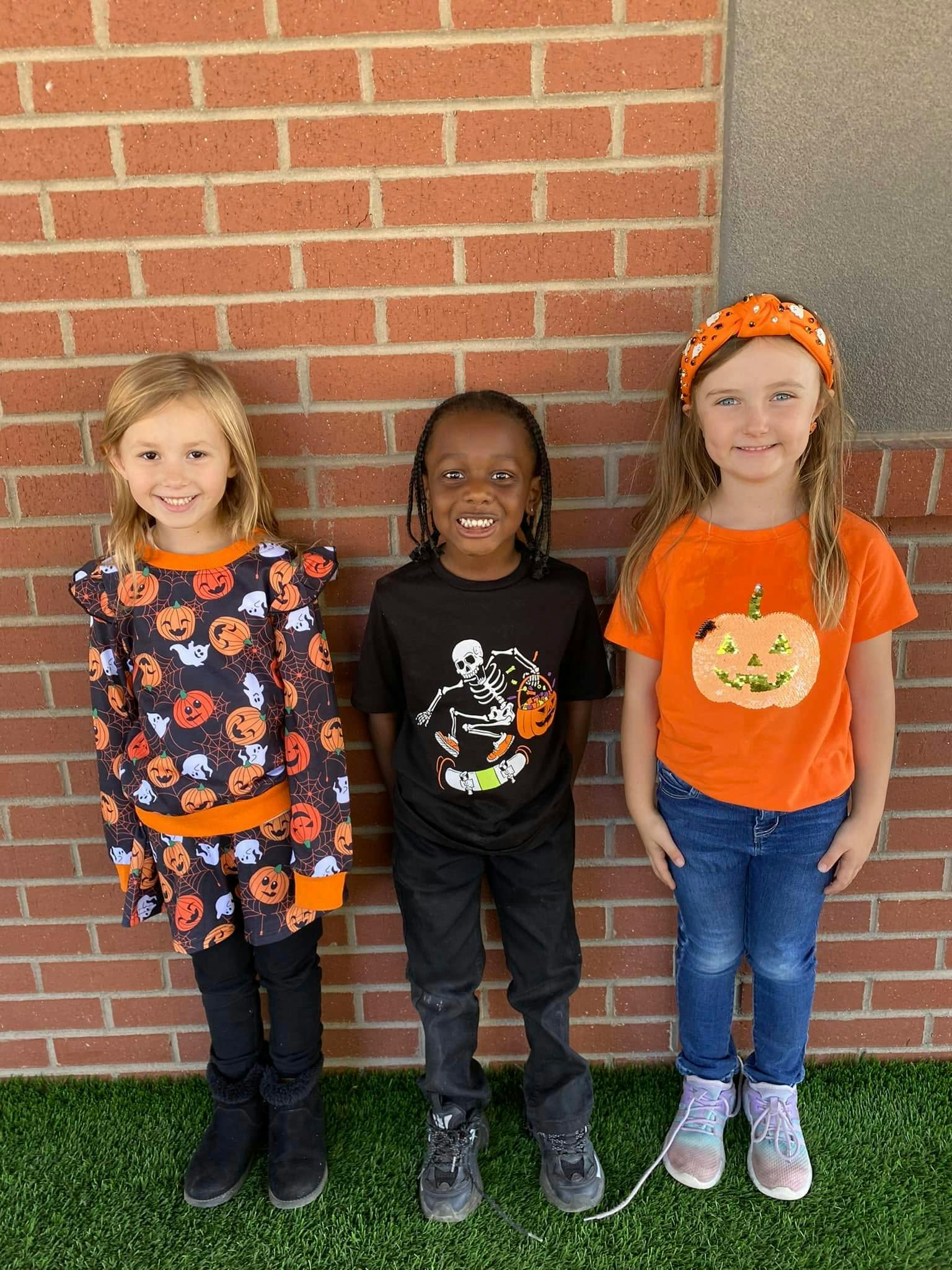 Three children in Halloween-themed clothing standing in front of a brick wall