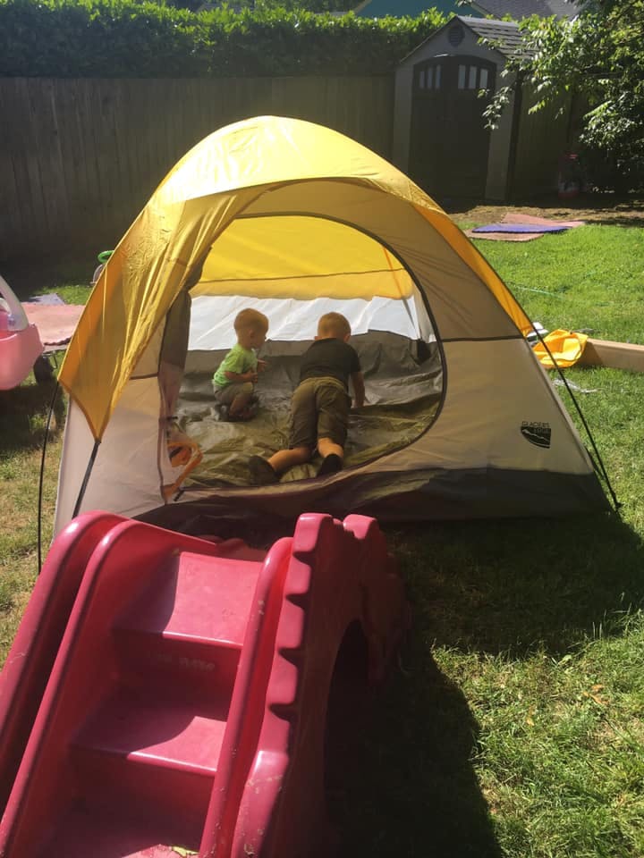 Two children playing inside a yellow tent in a grassy yard