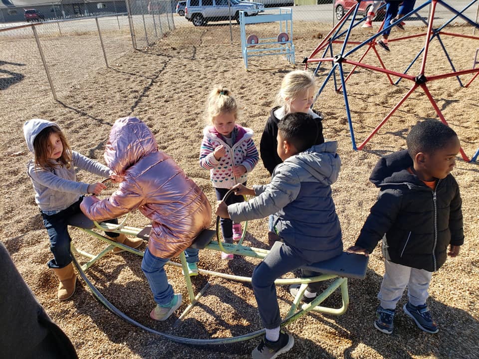 Children playing on a seesaw and standing on a playground