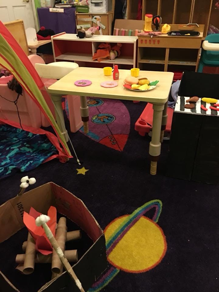 Playroom with a small table set with toy food, a tent, and a cardboard campfire