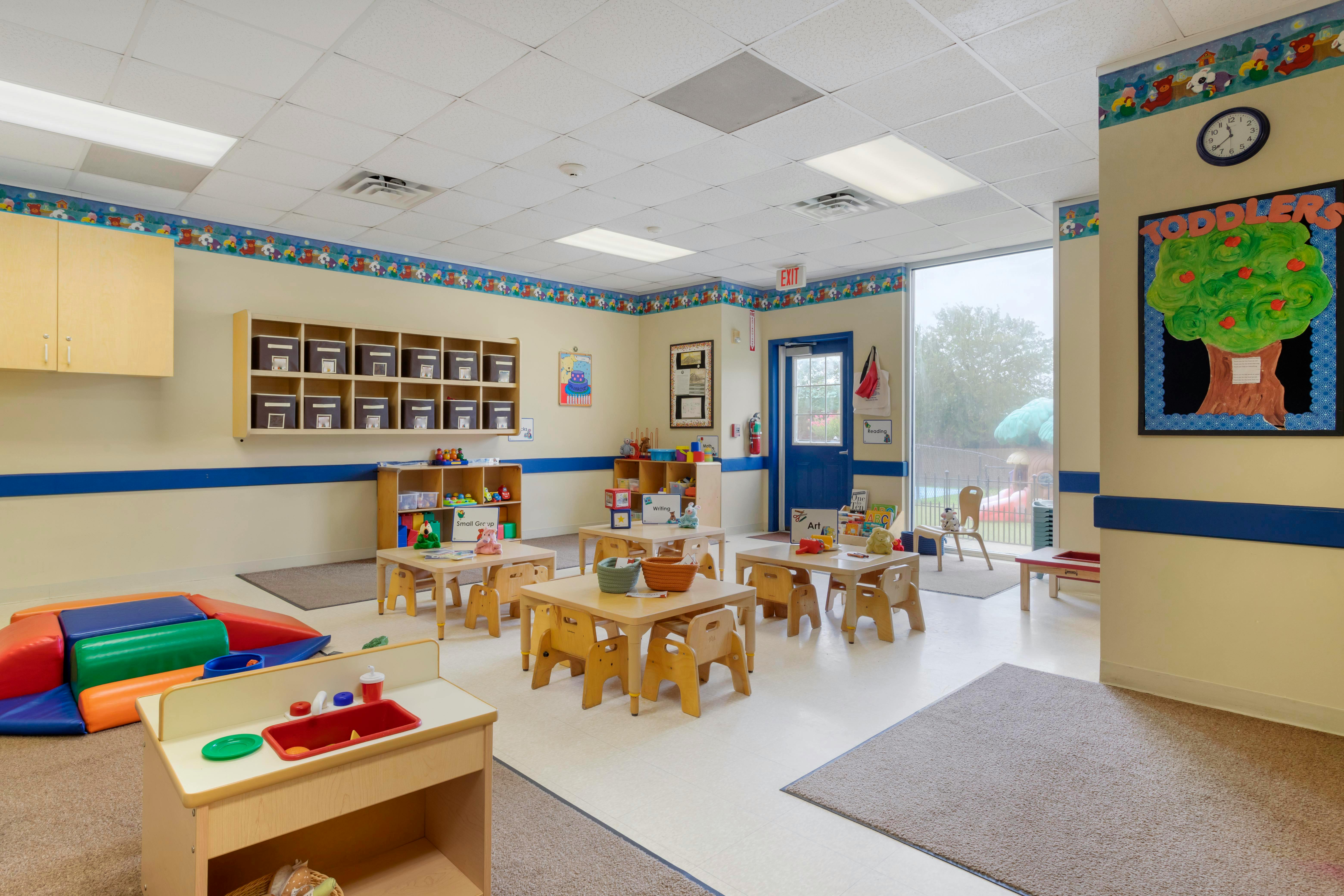 A colorful classroom with small tables and chairs, shelves, and a play kitchen