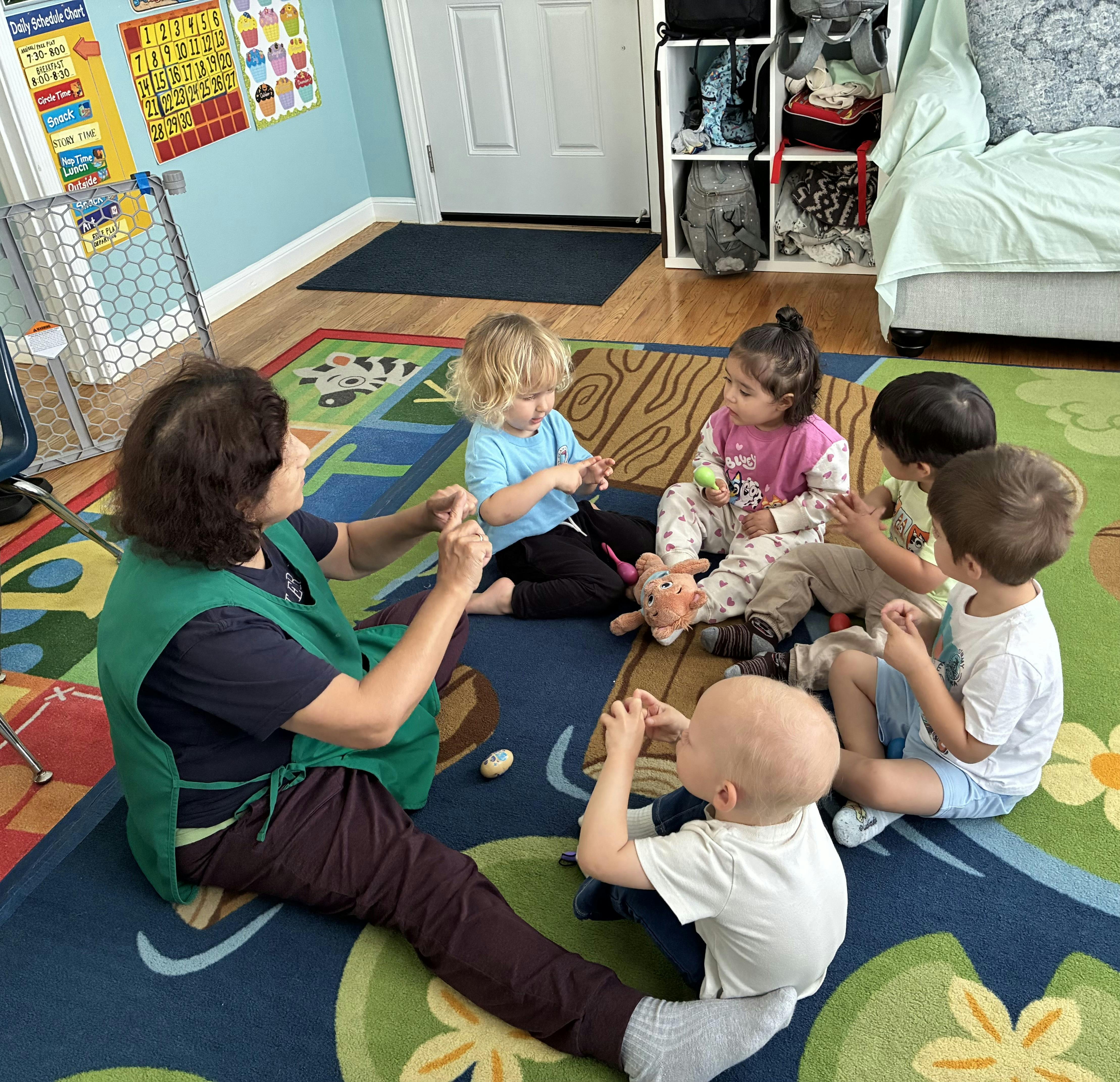 Adult and group of children sitting on a play rug in a classroom