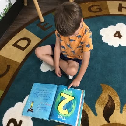 Child sitting on a rug, pointing at an open book with a large number two