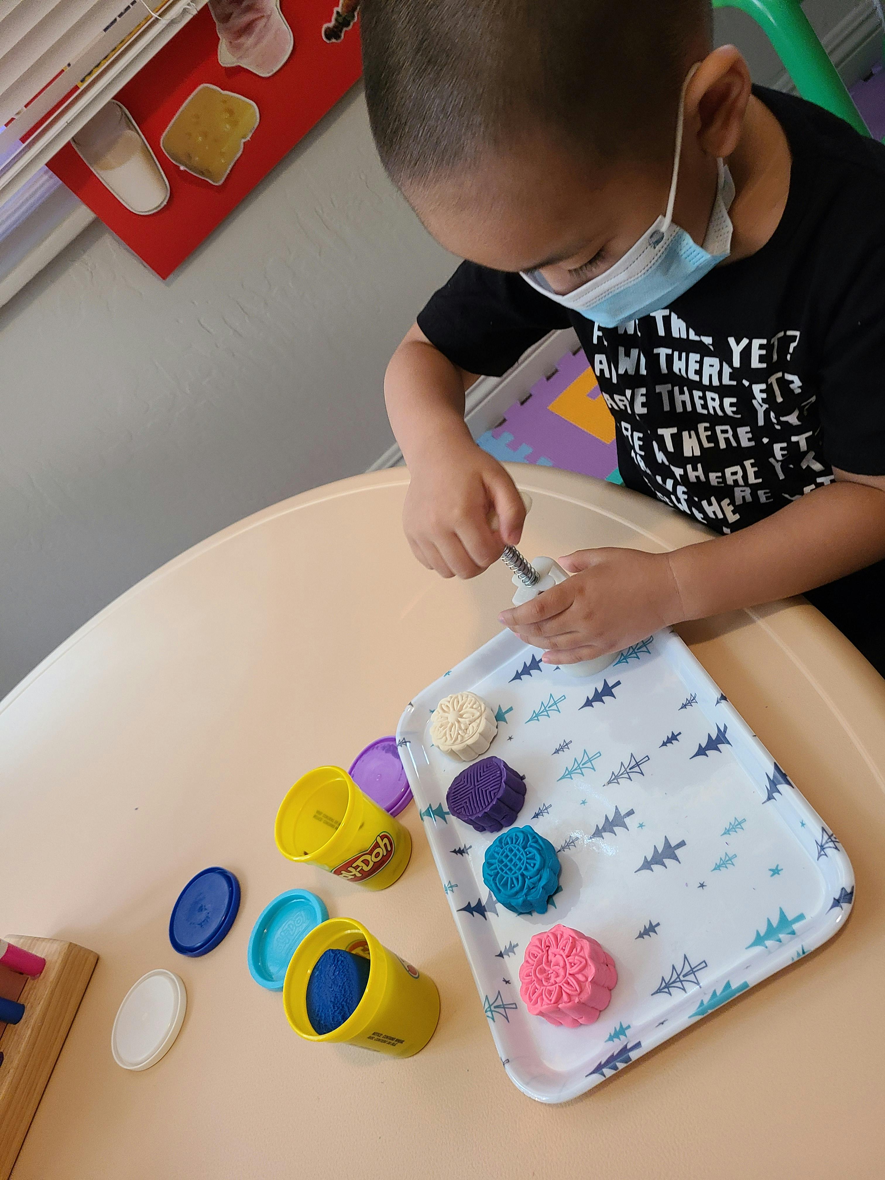 Child in a face mask playing with colorful playdough on a tray