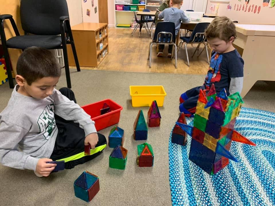 Two children playing with colorful magnetic building blocks on the floor