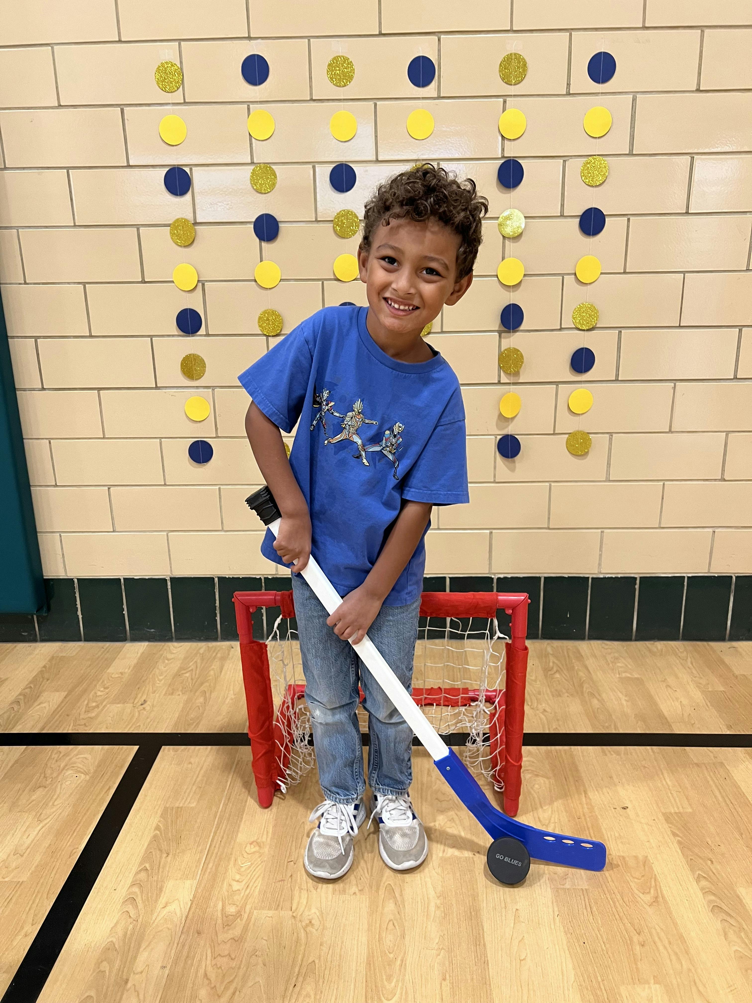 Child holding a toy hockey stick in front of a small goal