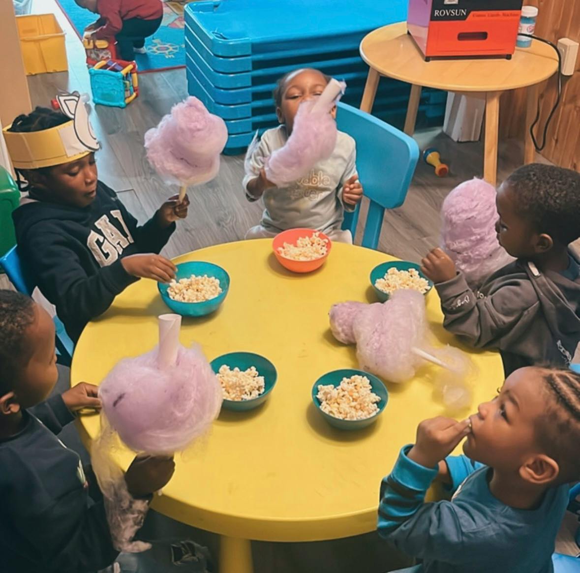 Children eating popcorn and cotton candy at a yellow table