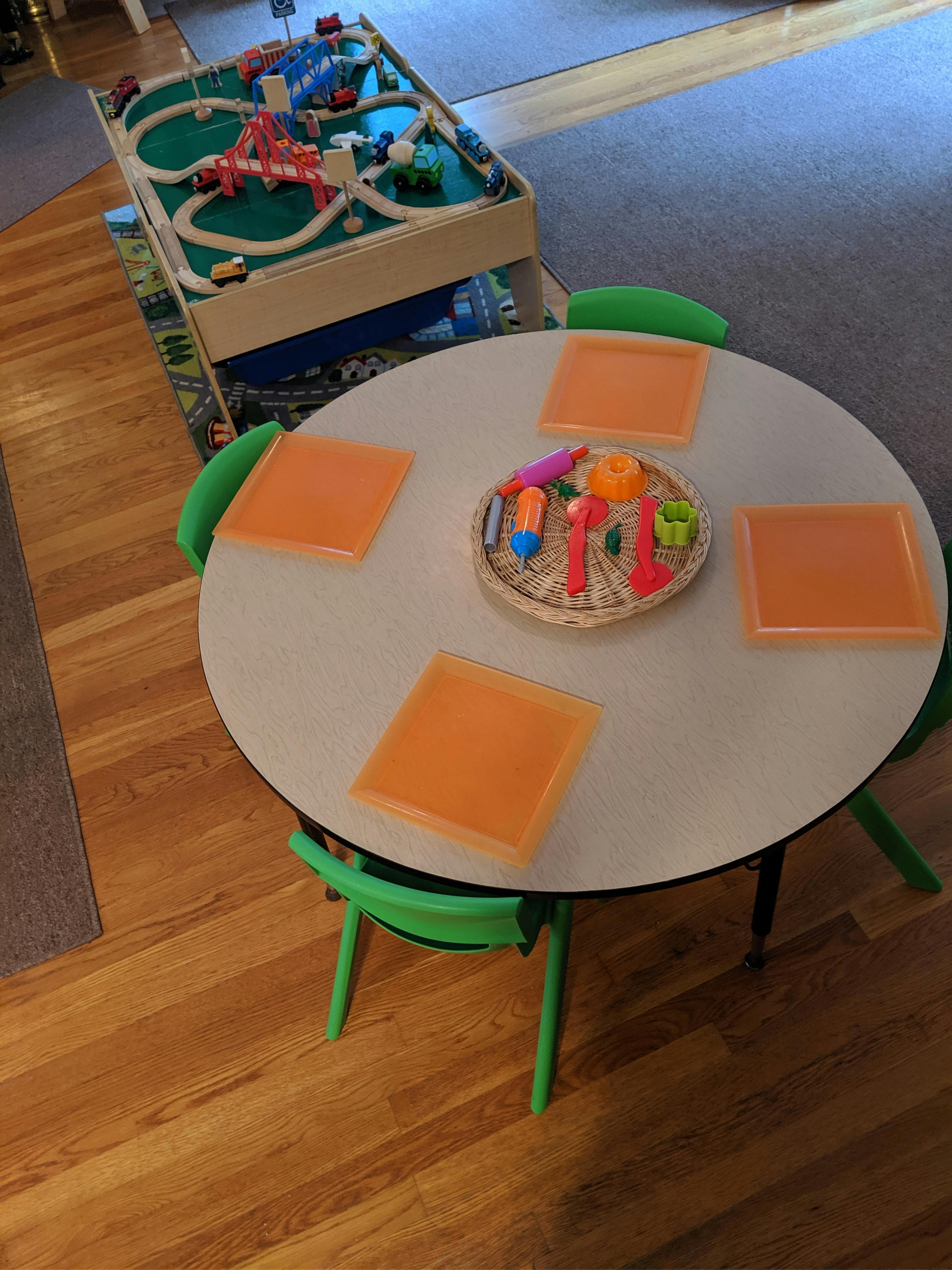 Children's table with playdough tools and a train set in the background
