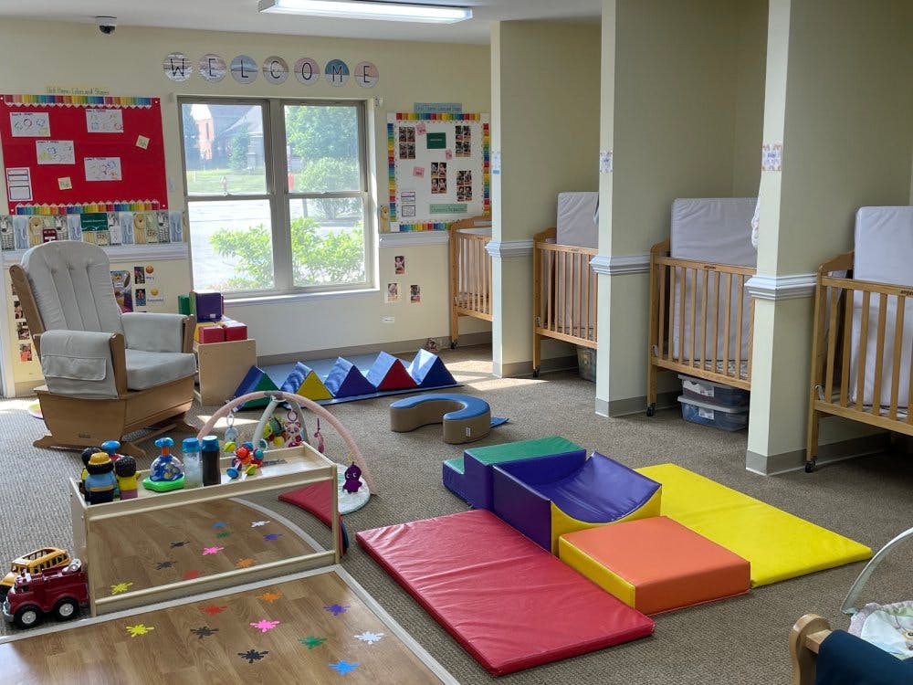 An empty nursery room with cribs, a rocking chair, and play mats