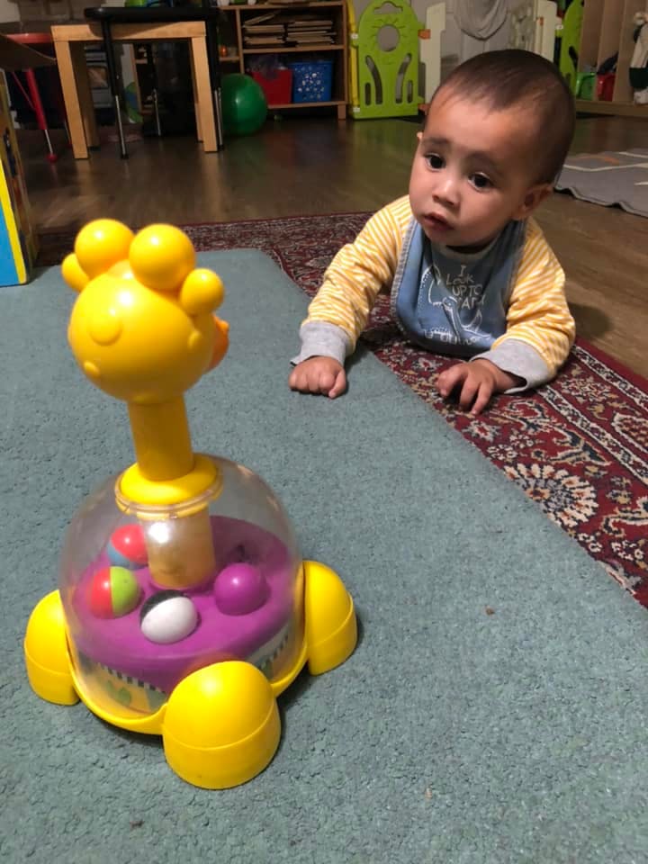Child crawling on a rug next to a yellow and purple toy