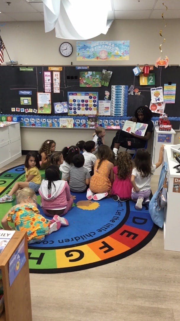 Person reading a book to children sitting on a rug in a classroom