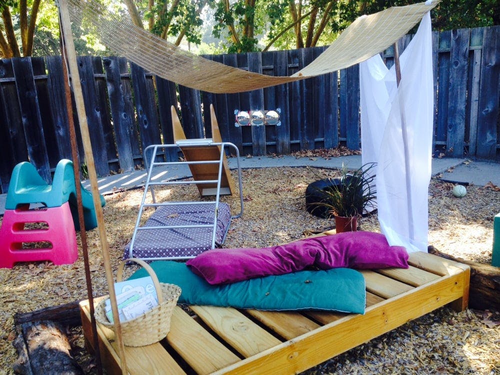 Outdoor play area with wooden pallet bed, cushions, and shade canopy
