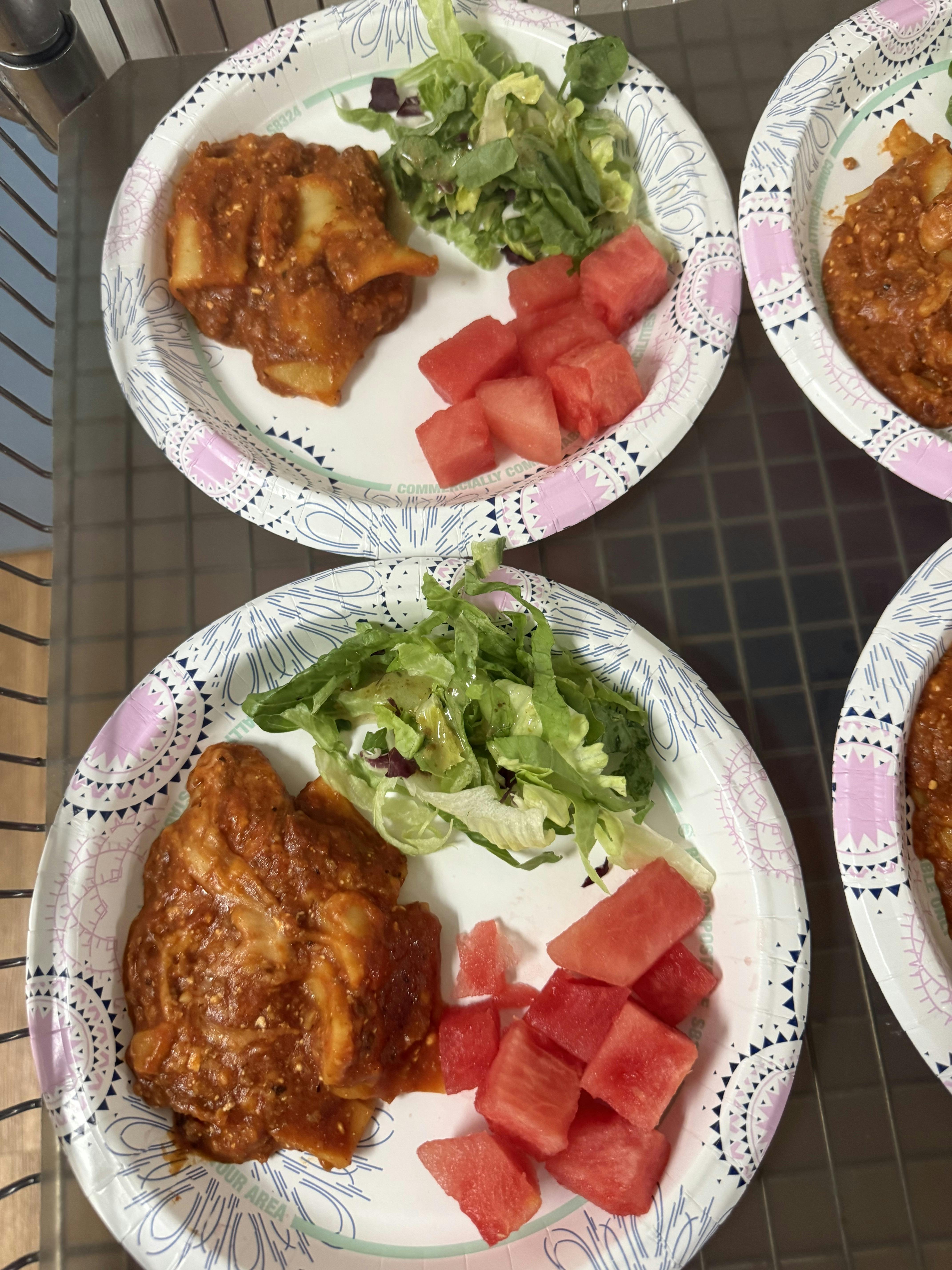 Paper plates with pasta in red sauce, green salad, and cubed watermelon