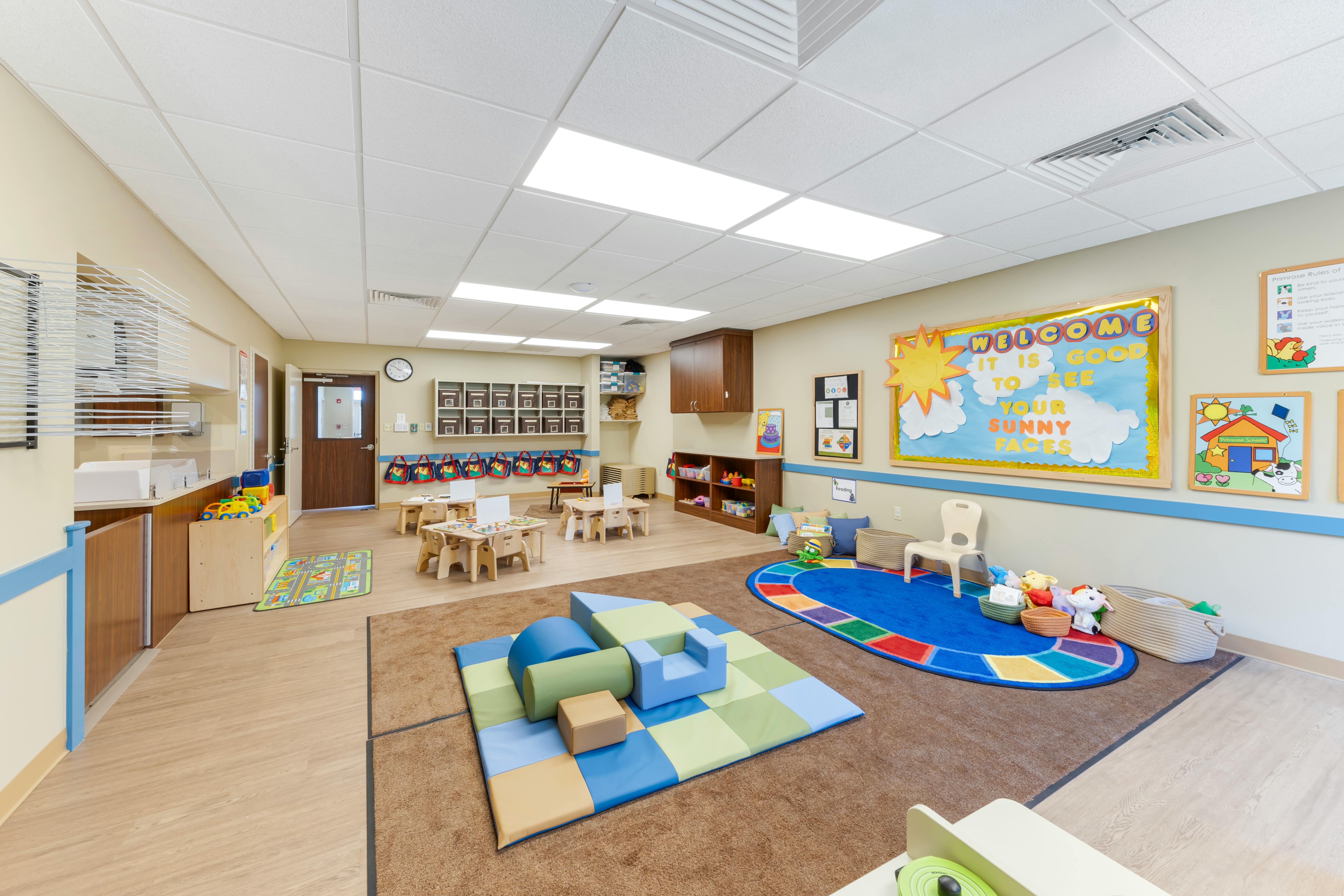 Classroom with small tables and chairs, play mats, and a "Welcome" sign