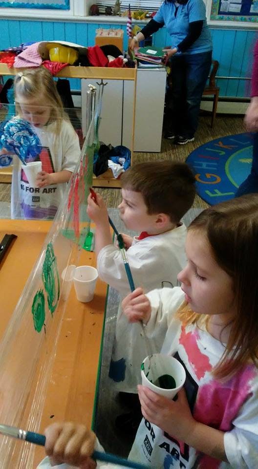 Children painting on a clear easel in a classroom