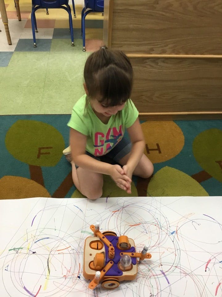 Child kneeling on floor watching a drawing robot
