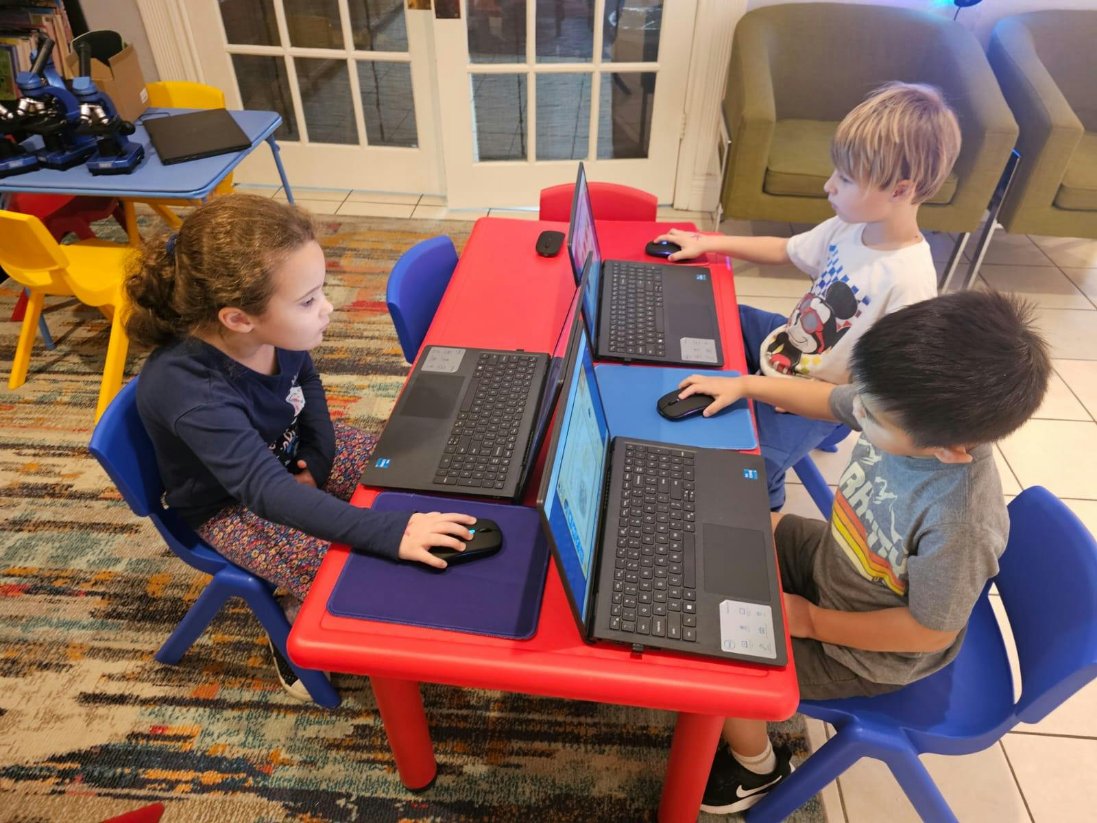 Three children using laptops at a red table