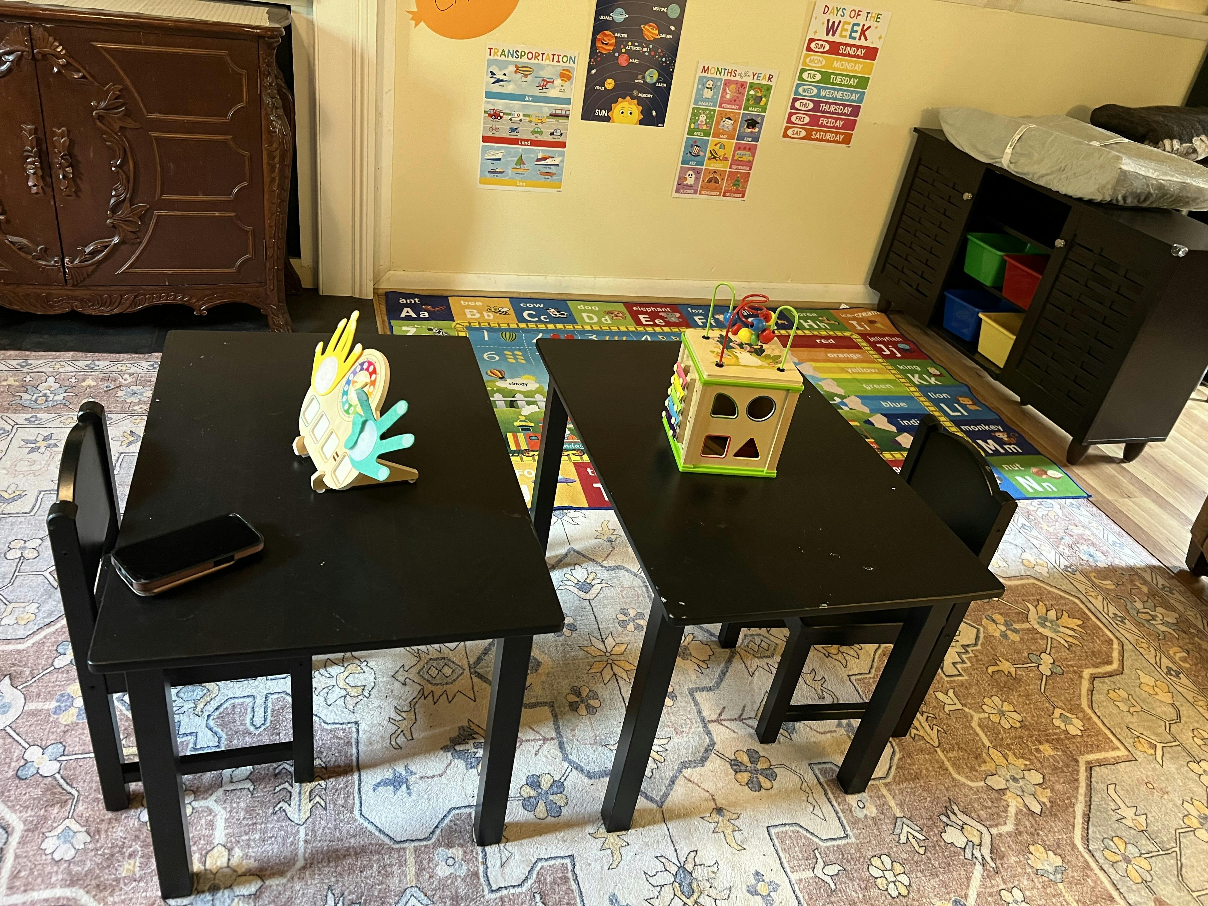 Two small black tables with child toys and educational posters in background