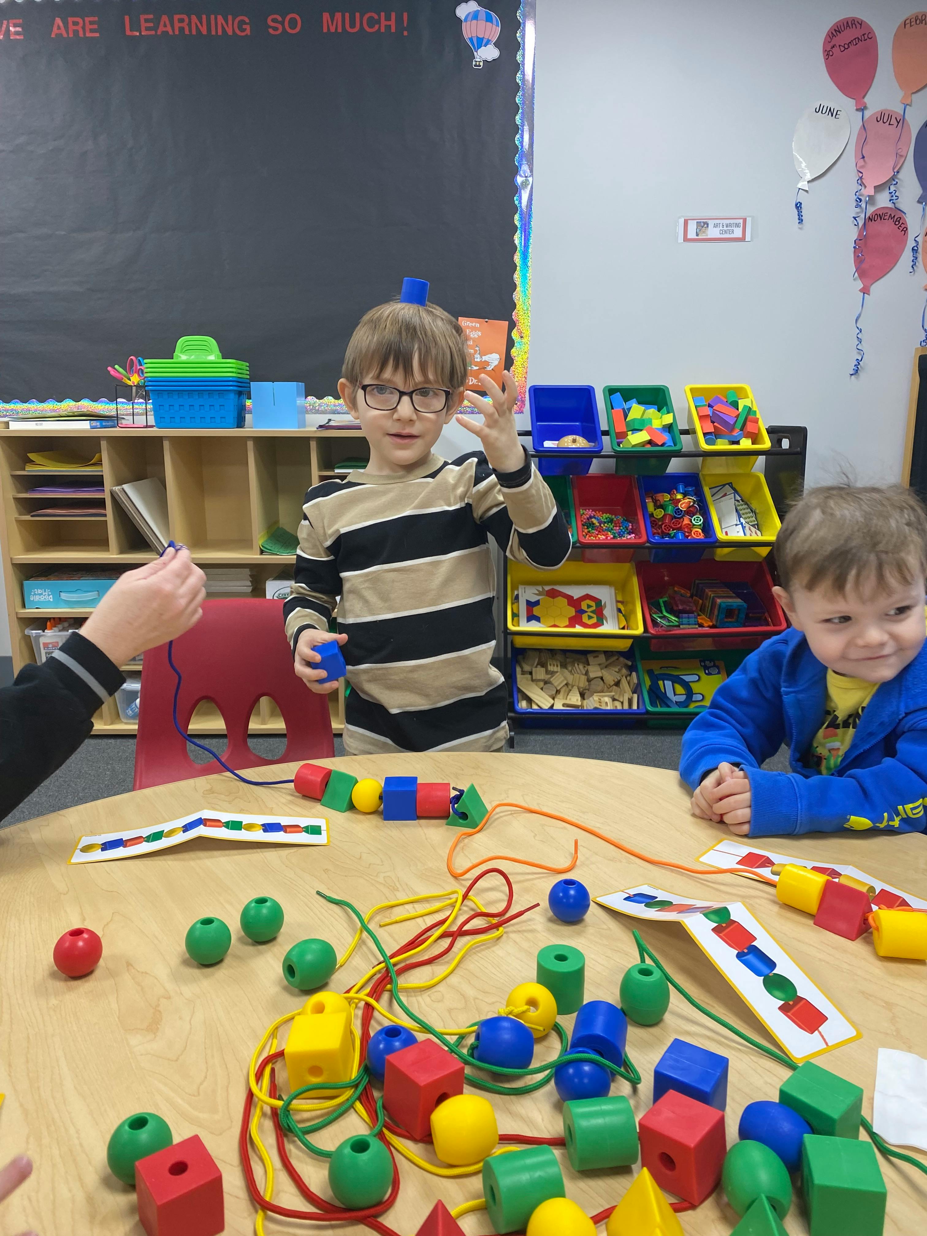 Two children and an adult at a table with colorful beads and strings