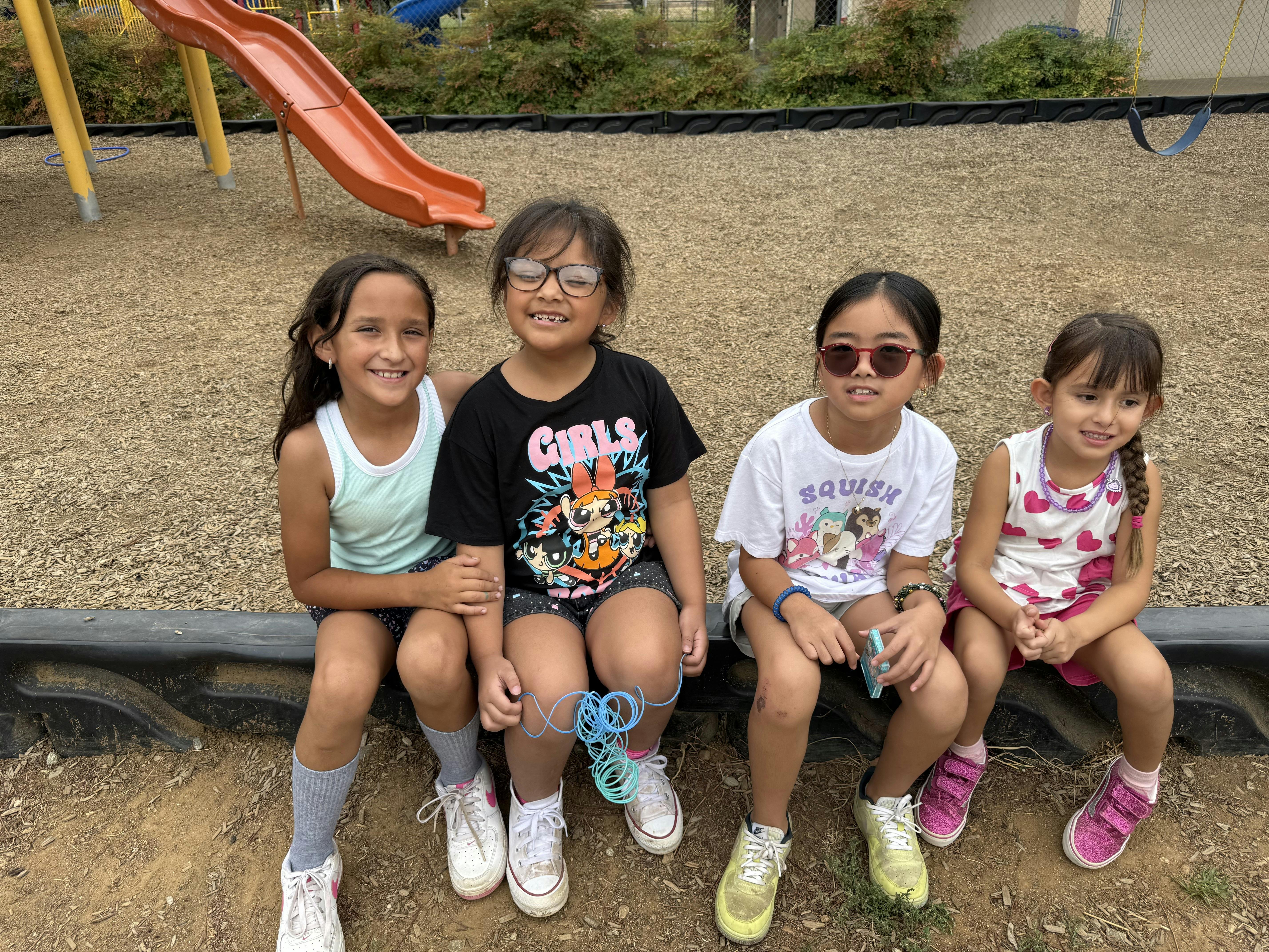 Four children sitting on a low wall on a playground