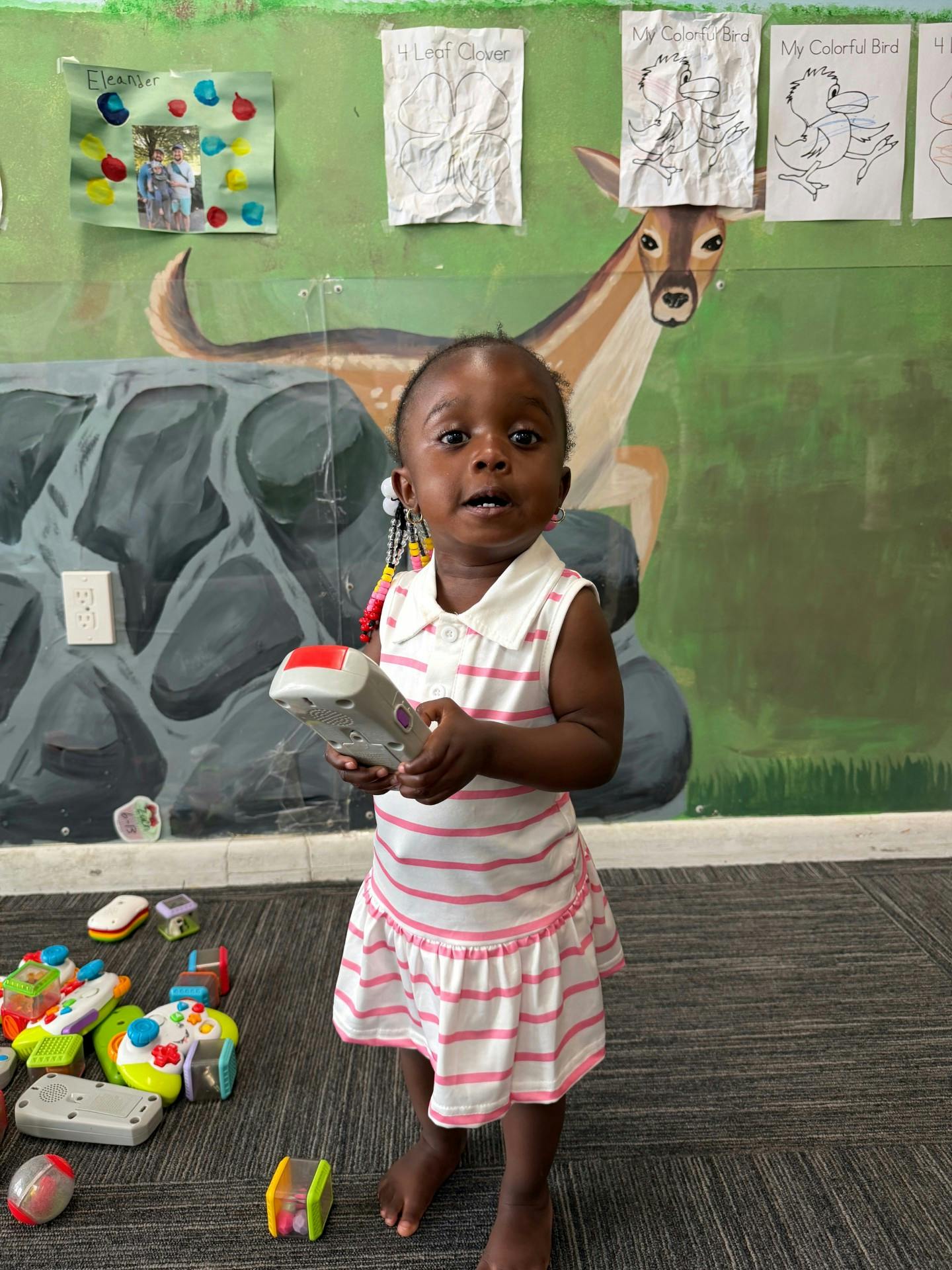 Child holding a toy remote control in a room with a deer mural