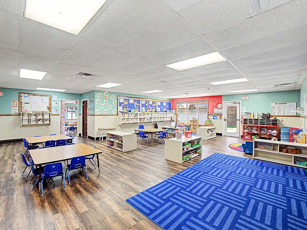 Empty classroom with small tables and chairs, and a blue patterned rug