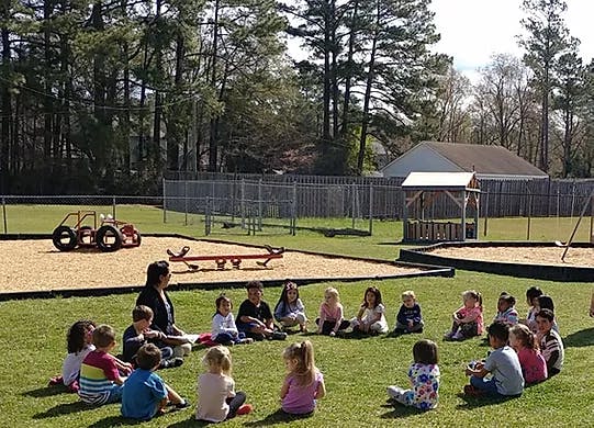Adult and children sitting in a circle on grass in a playground