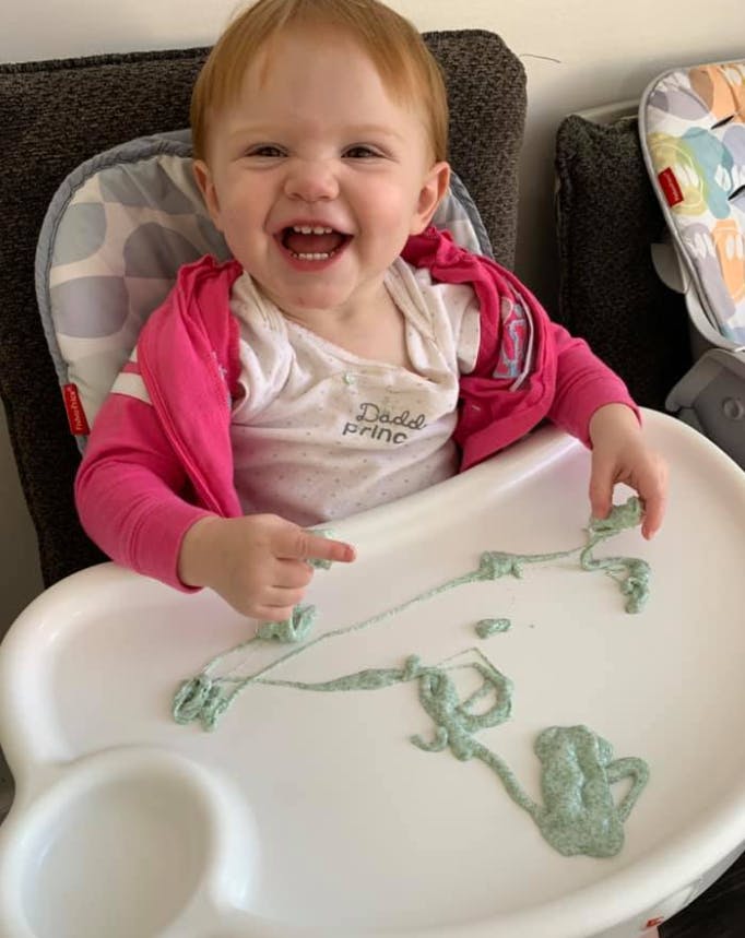Child in a high chair playing with green food on the tray