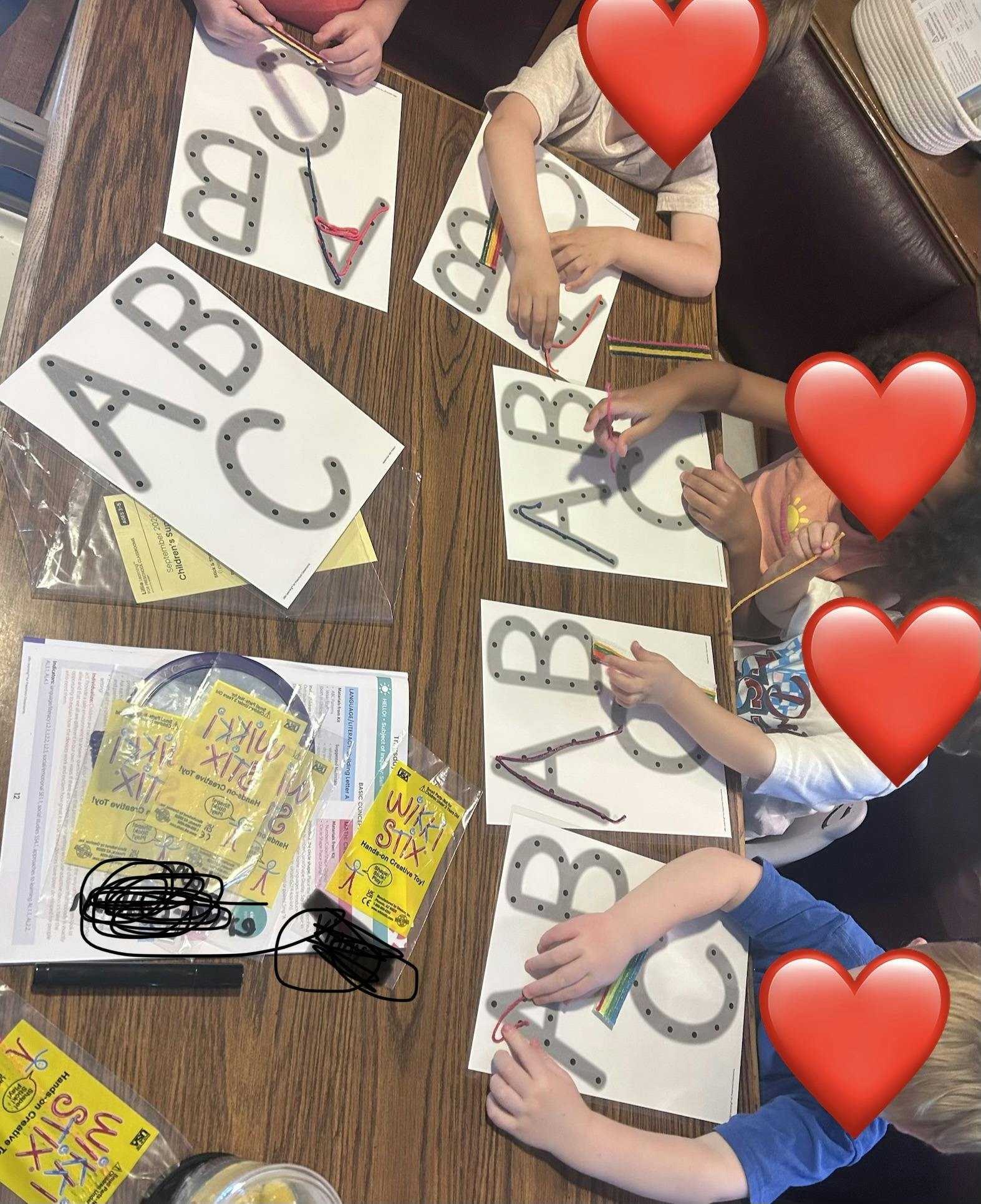 Children using wax sticks to trace alphabet letters on paper at a table