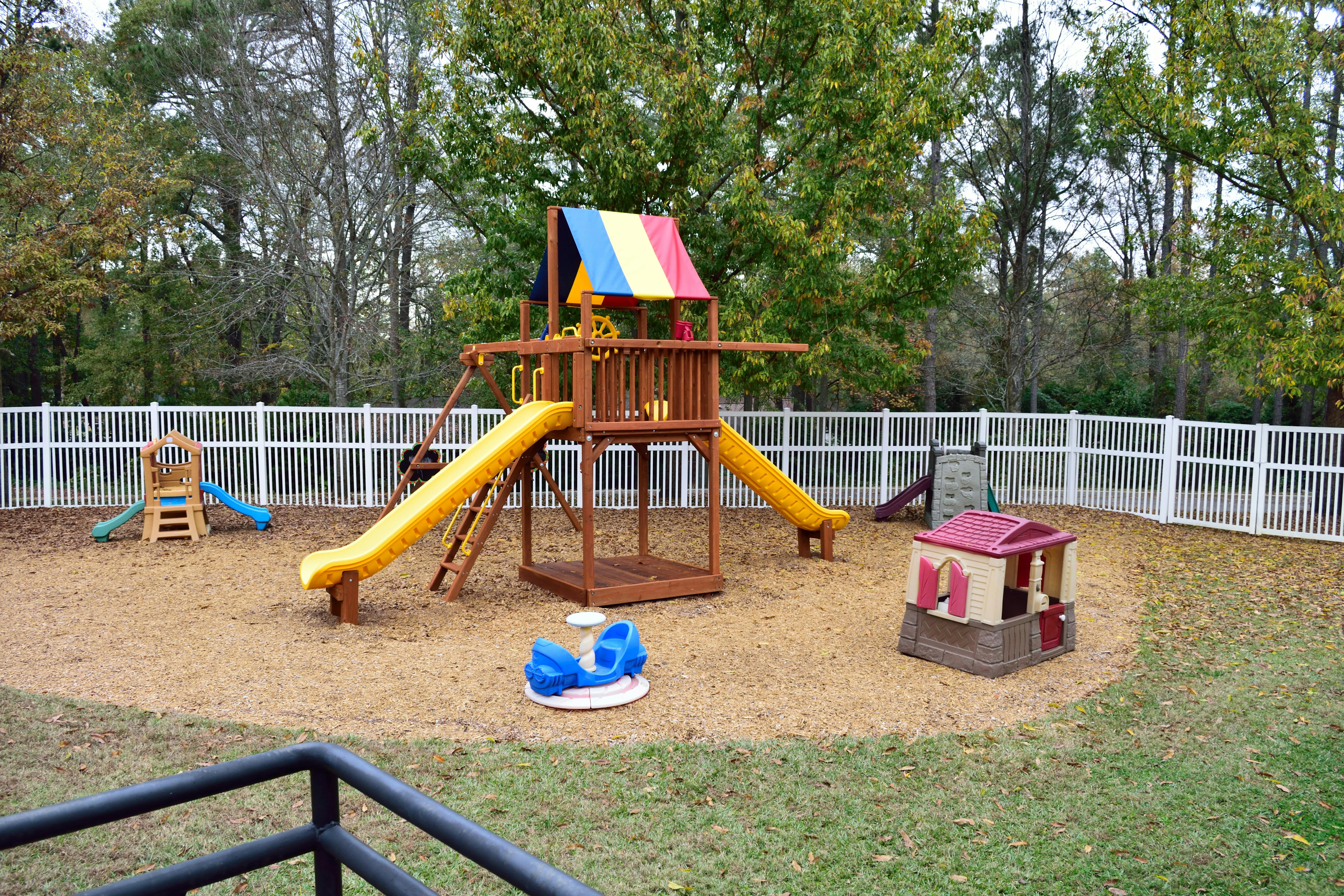 Playground with wooden playset, yellow slides, and a white fence